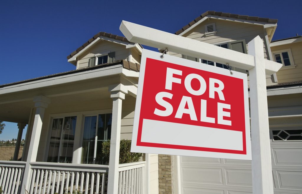 close up for sale sign with house in background